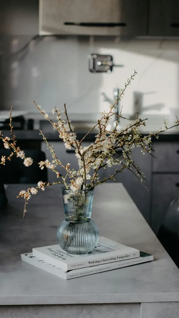 ribbed blue glass vase with white cherry blossom branches on stacked books on grey kitchen counter
