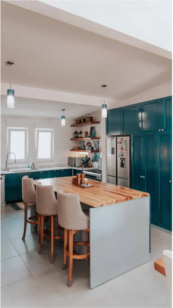 Deep teal kitchen cabinets with natural wood island and gray stools