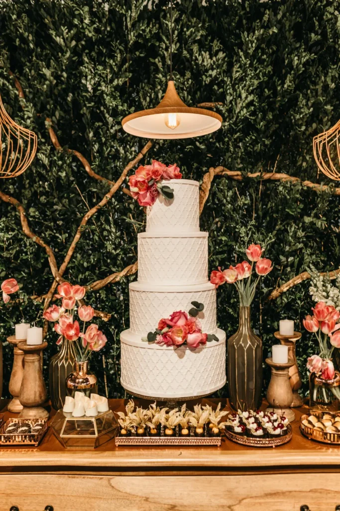 tall white tiered cake centerpiece surrounded by pink tulips and candles on dessert table setup
