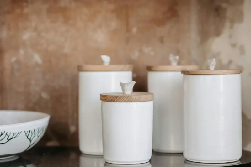 three matching white ceramic canisters with wooden lids on kitchen counter for clean organized look
