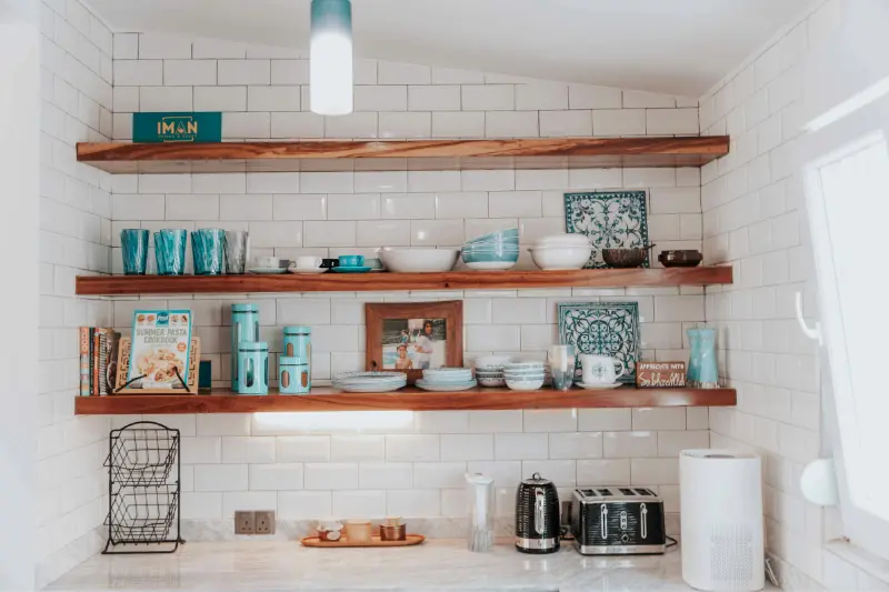 open kitchen shelves with teal and white dishes on white subway tile wall
