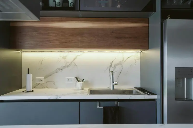 modern kitchen with warm LED strip lights under wood cabinet illuminating marble backsplash and white countertop