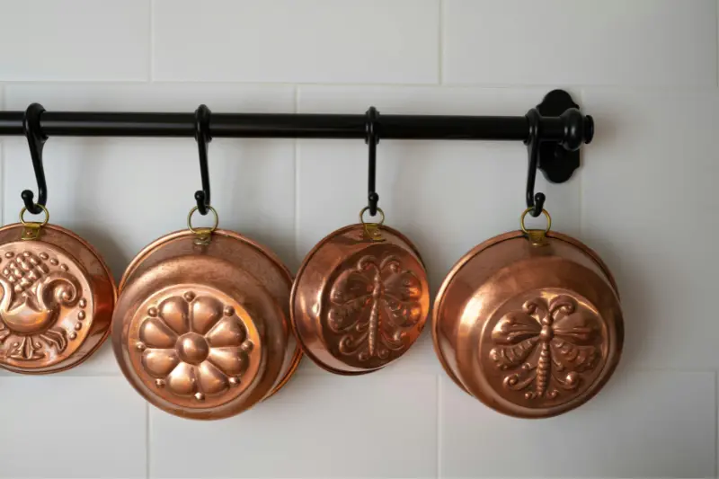 four copper pots hanging on black wall mounted rail against white subway tile in small kitchen