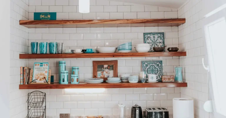 Open floating wooden shelves with turquoise kitchenware on a white subway tile wall for small kitchen space-saving decor.