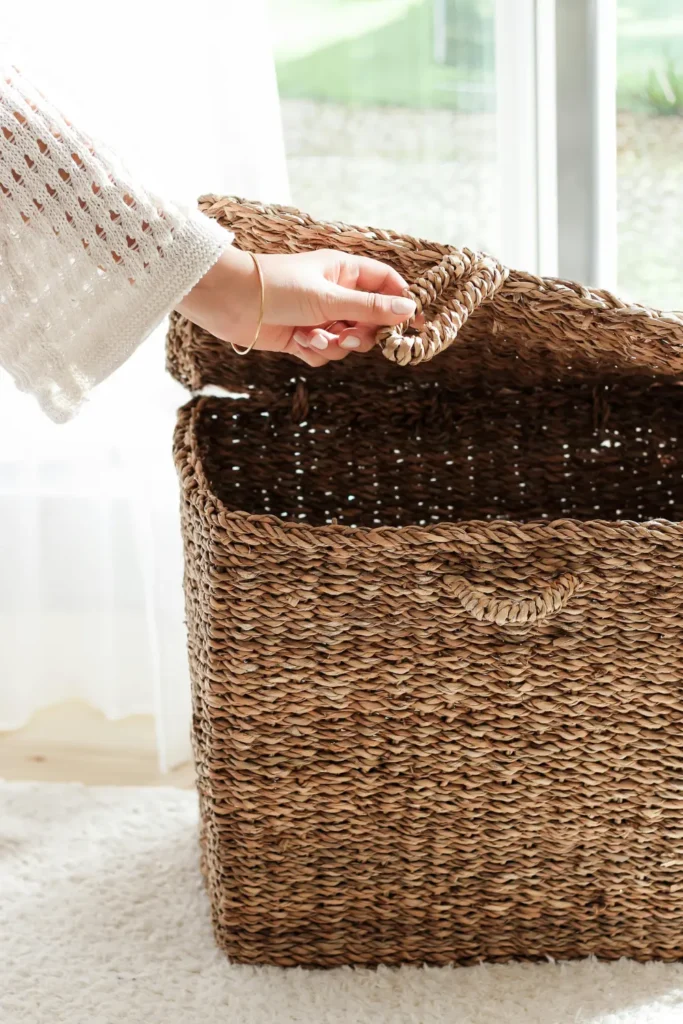 large woven seagrass basket with lid being opened by a hand in bright natural light showing storage solution for outdoor spaces