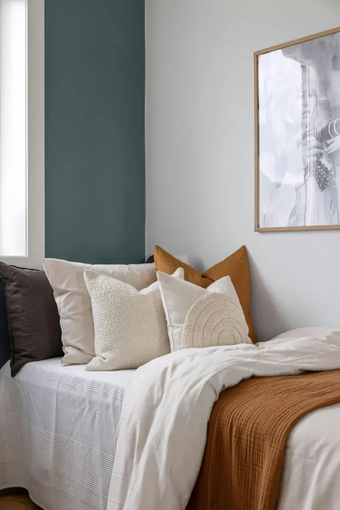 bed styled with layered decorative pillow covers in cream beige rust and charcoal tones against a teal and white bedroom wall with a framed print above
