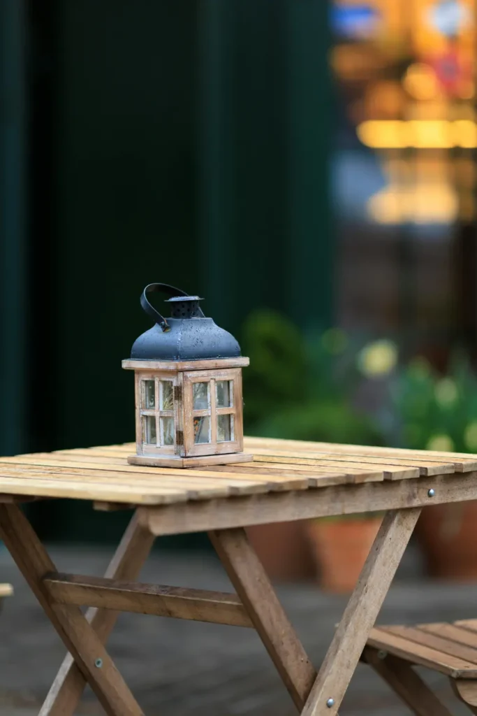 rustic wooden and metal outdoor lantern sitting on a wooden folding table on a patio with blurred garden background