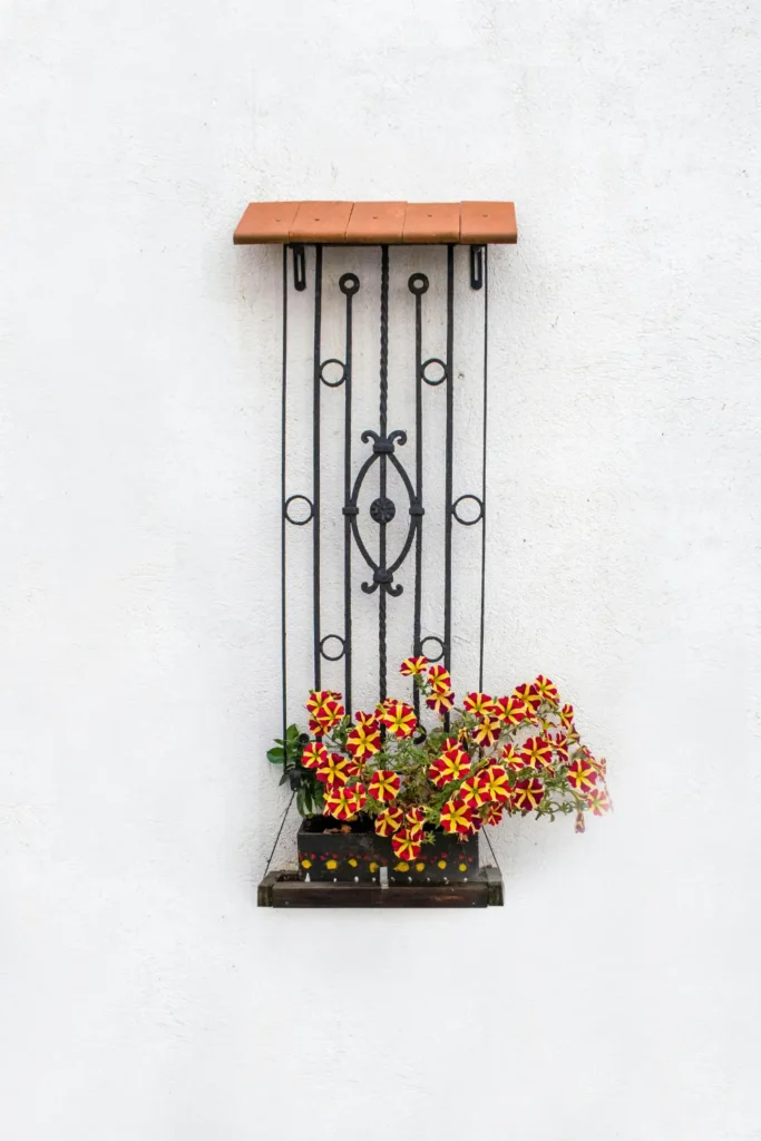 single wall mounted iron planter with bright red and yellow flowers mounted on a clean white outdoor wall