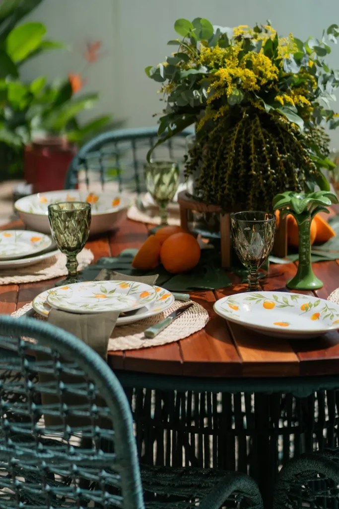 outdoor dining table styled with matching botanical orange patterned plates green glasses and woven placemats on a wooden round table with floral centerpiece