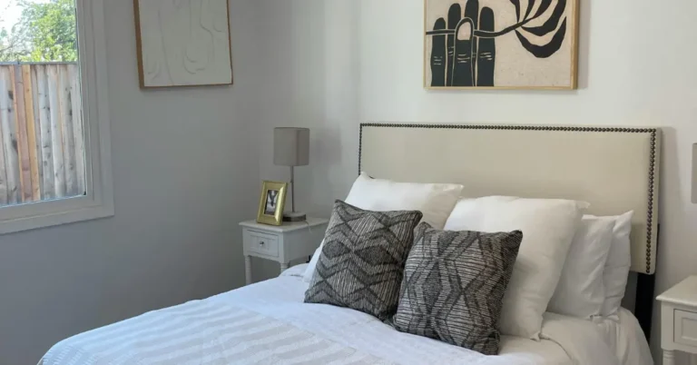 A cozy modern bedroom with neutral decor, featuring a white bed with patterned throw pillows, a cream tufted headboard, and minimalist wall art, illustrating beautiful bedroom decor ideas.