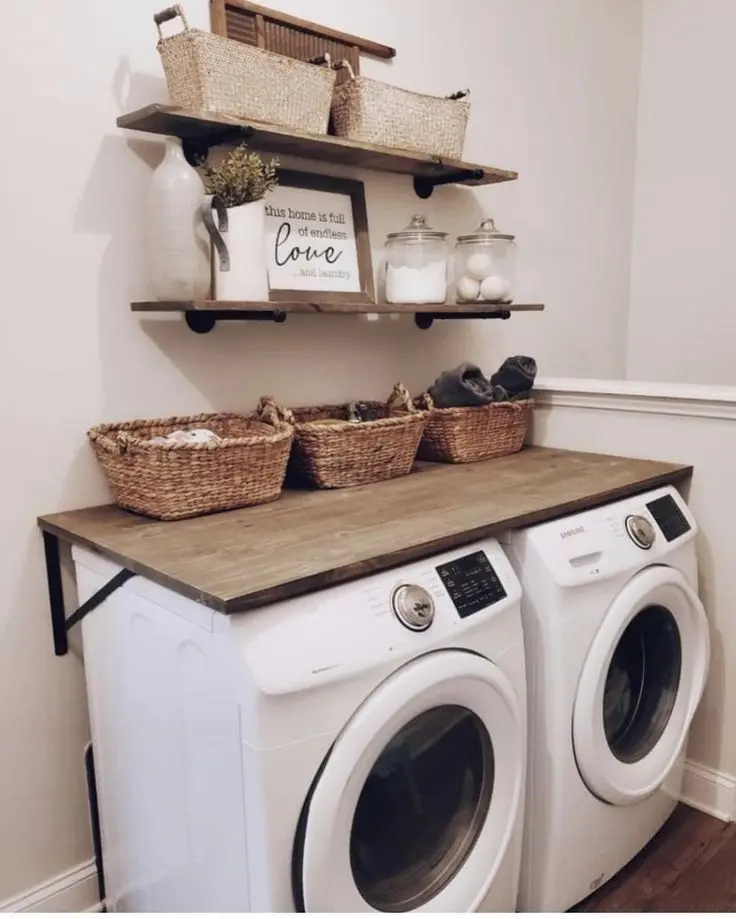 Small laundry room with a wooden folding station countertop above a washer and dryer, woven baskets on top and rustic open shelving above with glass jars and decor.