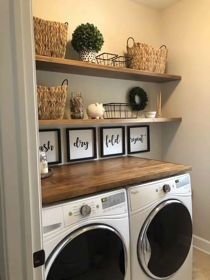 Small laundry room with open wood shelving filled with woven baskets and decor above a wooden folding countertop and side by side washer and dryer.