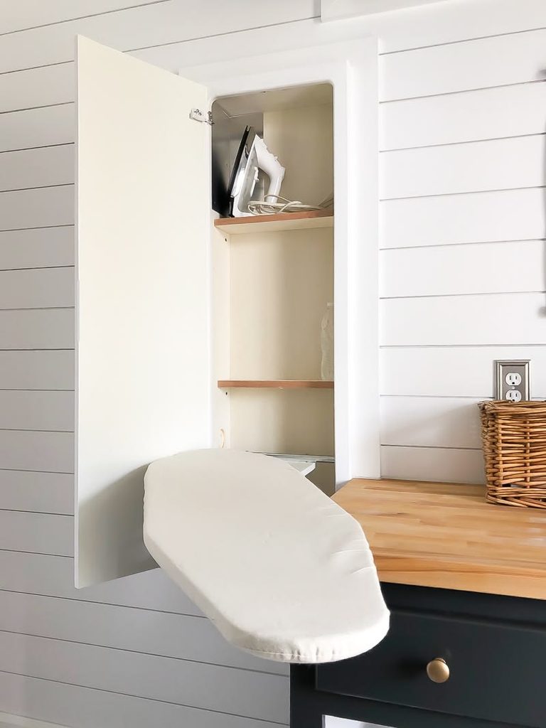 Built-in cabinet with a fold-down ironing board open beside a wood countertop and wicker basket in a small laundry room