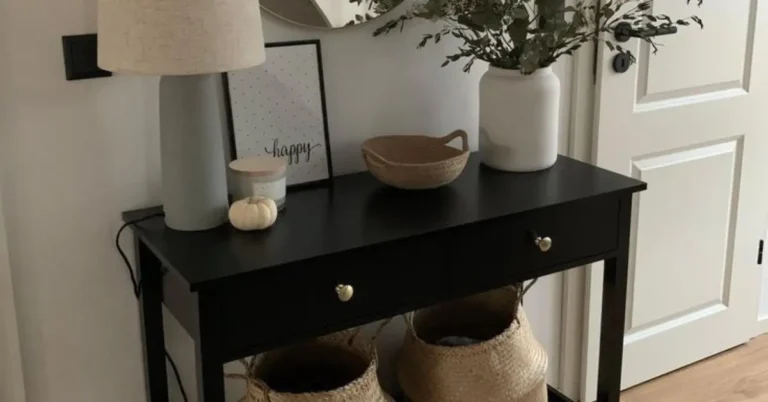 Small apartment entryway with a black console table styled with a linen lamp, white vase with eucalyptus stems, woven basket tray and belly baskets underneath by a white door
