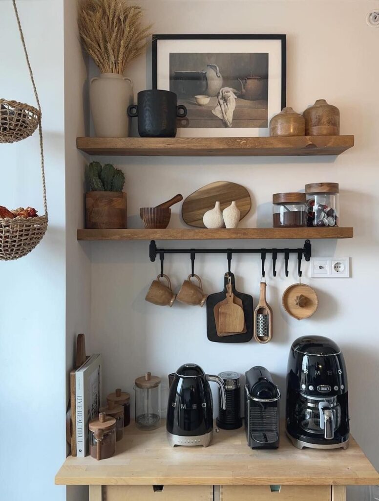A white SMEG coffee machine setup with a coffee bar love is brewing sign mounted above floating wooden shelves holding mugs and canisters in a small kitchen