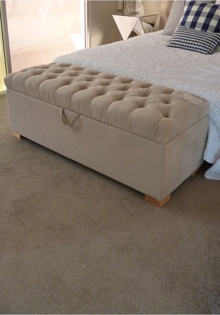 Tufted beige storage bench with a lift-top lid at the foot of a bed with navy checkered pillows in a small apartment bedroom