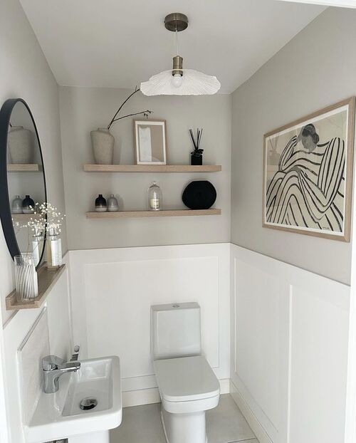 Minimalist bathroom with two floating shelves above toilet holding matching neutral ceramic vessels and vases in beige and grey tones