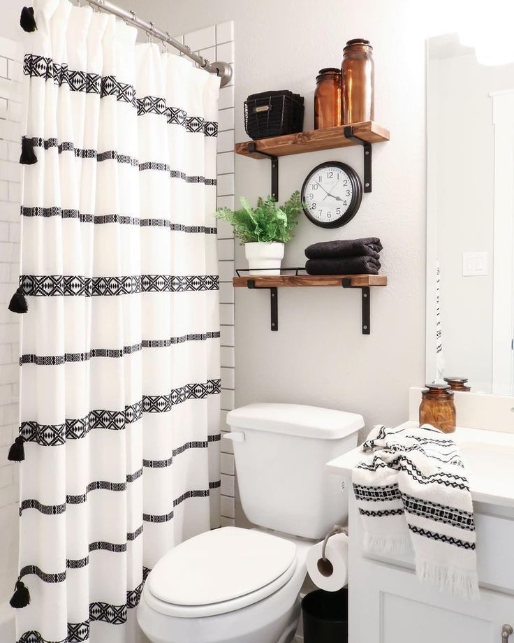 Small apartment bathroom with a black and white striped shower curtain with tassels, wood floating shelves, black towels and a small green plant