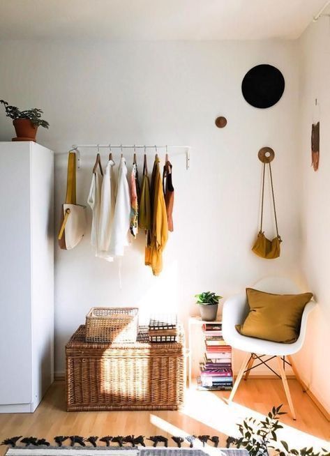 Small apartment bedroom with a wall-mounted clothing rod holding colorful hanging clothes above a large woven storage trunk