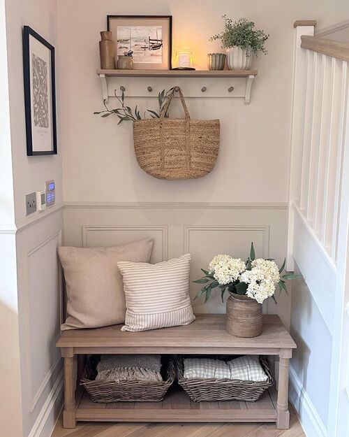 Small apartment entryway with a wood bench, cushions, woven baskets underneath, shelf with decor above and a hook with a woven bag
