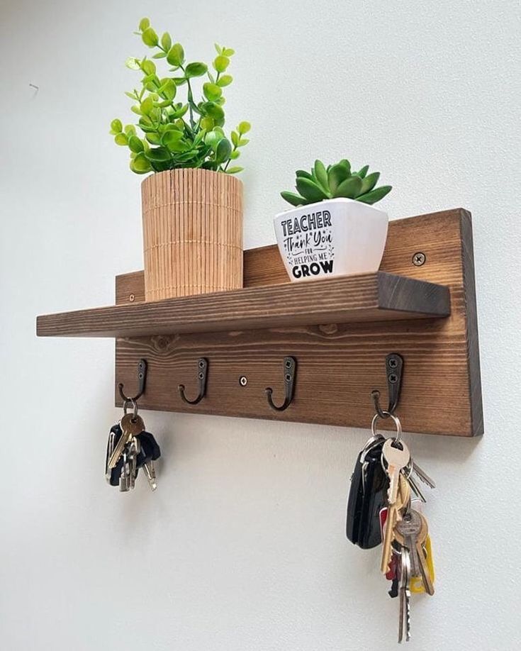 Small apartment entryway wooden wall mounted key holder with black hooks, small shelf styled with potted green plants and keys hanging below