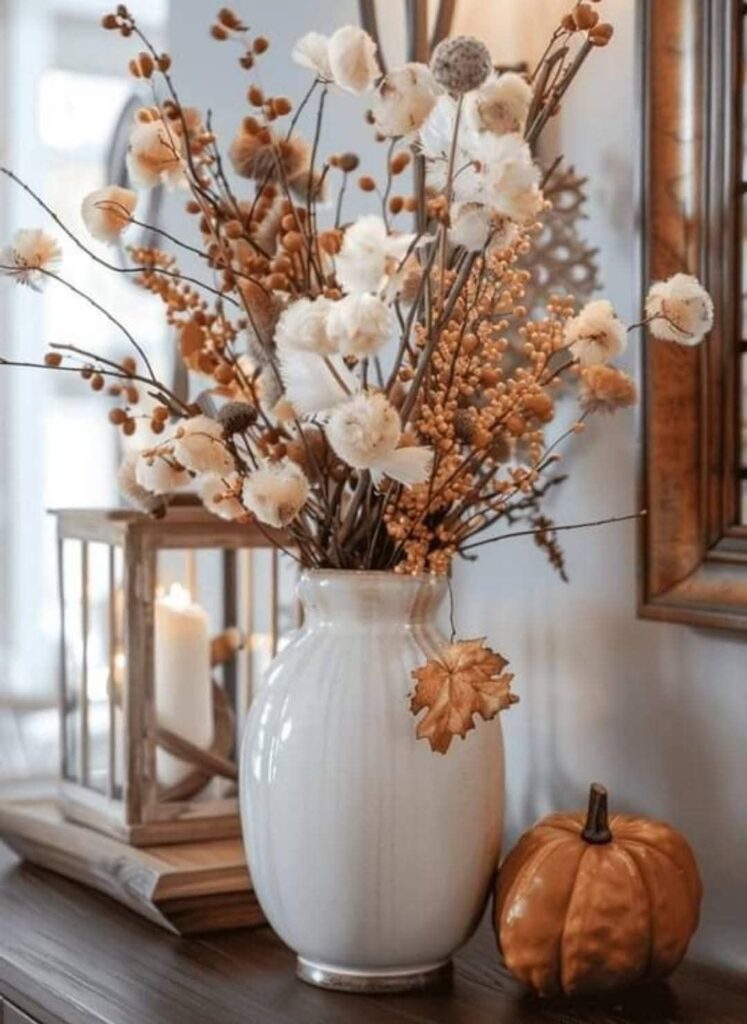 White ceramic vase with dried stems and a small pumpkin styled on an entryway table
