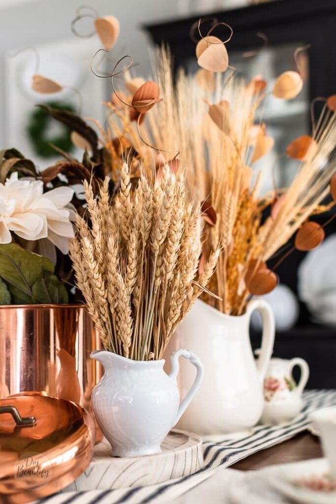 Wheat stalks in a white ironstone pitcher next to a copper bowl for a fall centerpiece