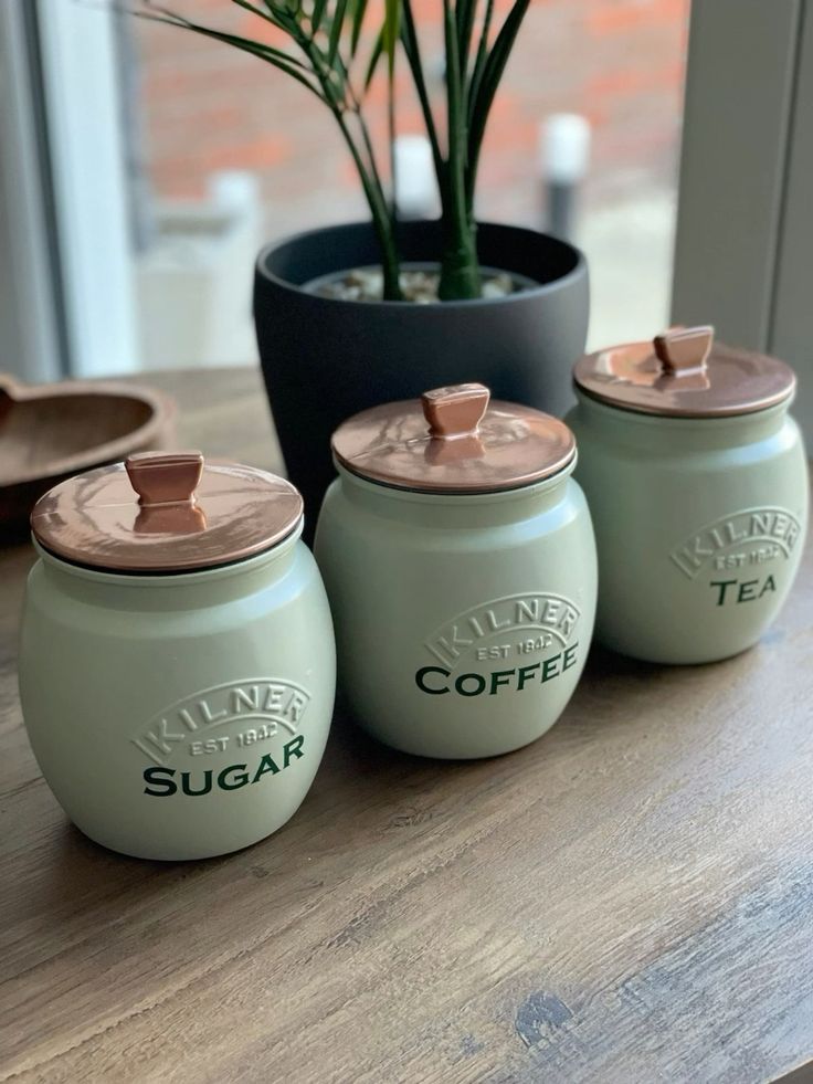 Sage green Kilner canisters labeled sugar, coffee, and tea on a kitchen counter