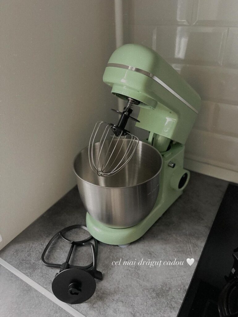 Sage green stand mixer with whisk attachment on a kitchen counter corner