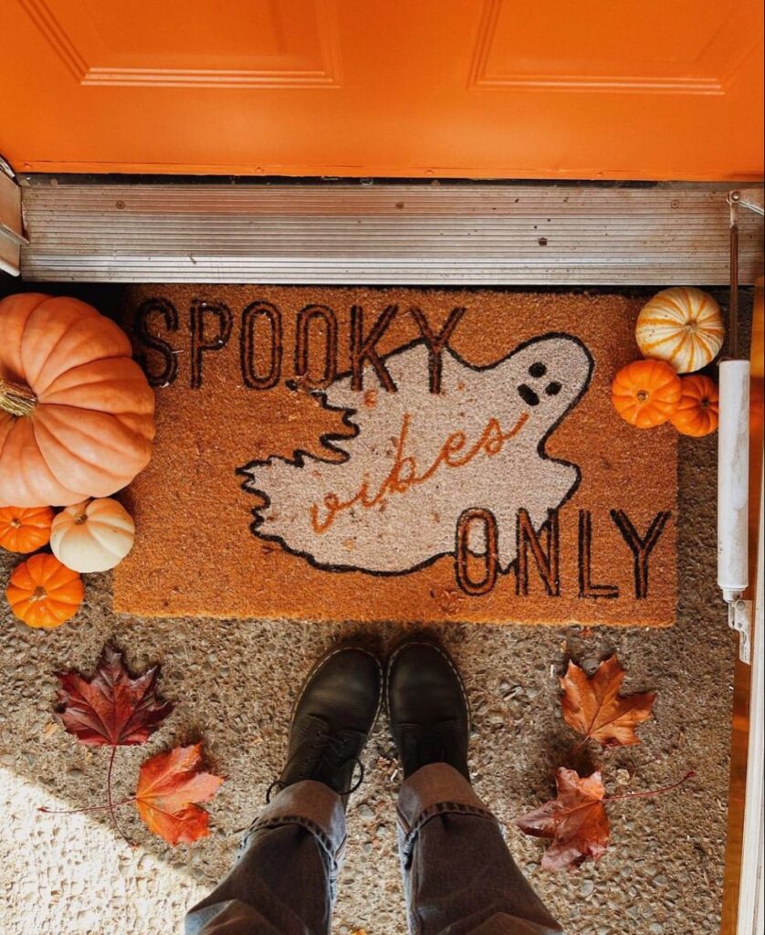 Ghost-print Halloween doormat with small pumpkins and fall leaves at a front door