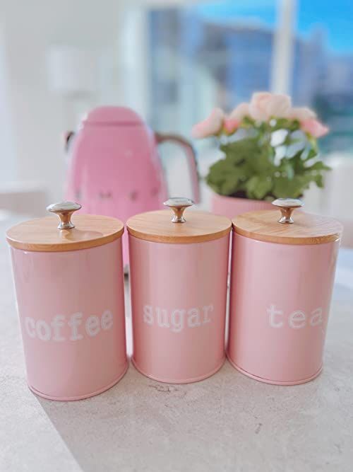 Pink metal canisters labeled coffee, sugar, and tea with wood lids on a counter