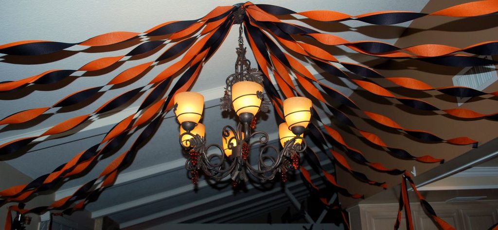 Black and orange tissue paper streamers draped from a ceiling light fixture for vintage Halloween decor