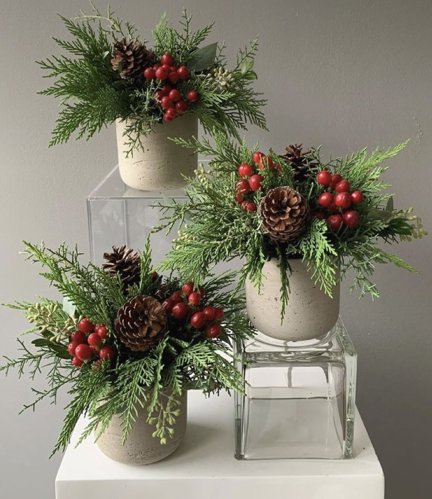 Three cement and glass bud vases with greenery, pinecones, and red berries as a winter centerpiece
