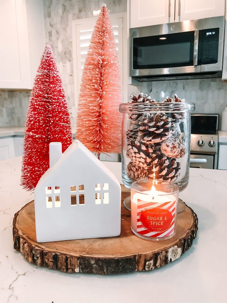 Red and pink ombre bottle brush trees with a ceramic house and pinecone jar winter centerpiece