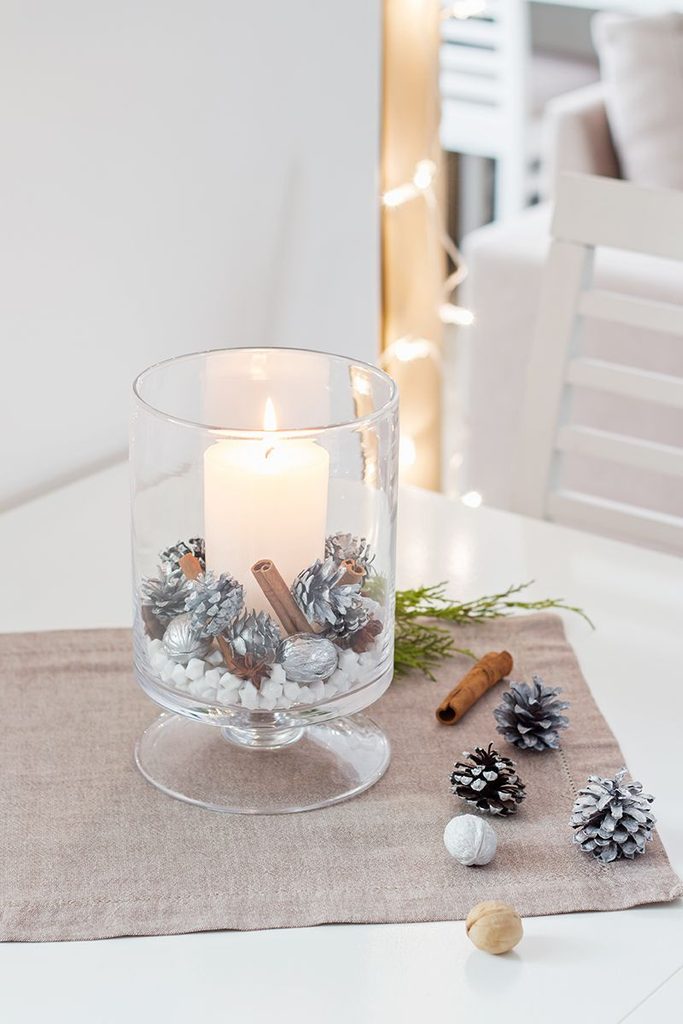 Silver painted pinecones and a pillar candle inside a glass hurricane vase winter centerpiece