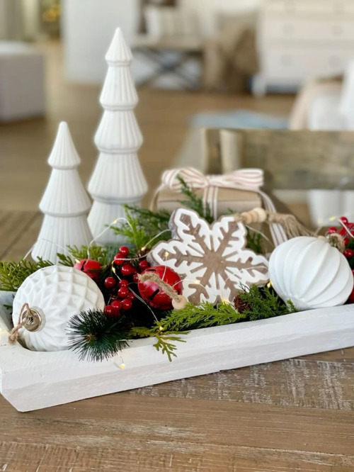 White ceramic trees, ornaments and red berries with greenery in a white tray on a wood coffee table