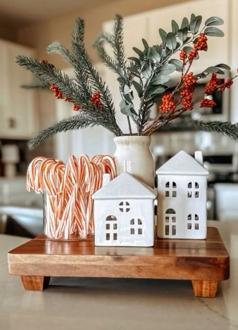 Vase of pine and red berry branches with candy canes and two white houses on a wood tray