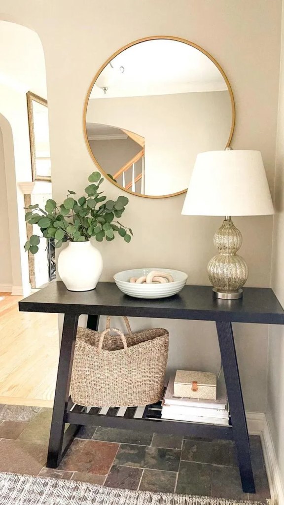 narrow black console table with a round gold mirror and a vase of eucalyptus, small entryway table decor