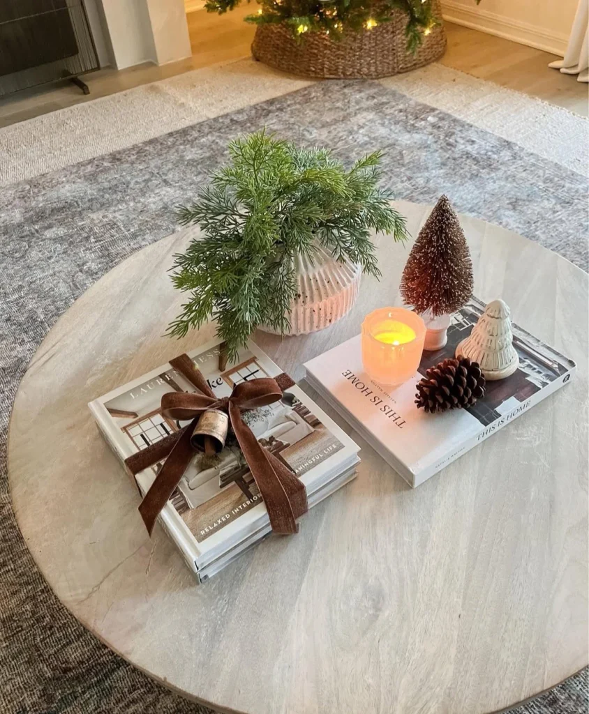 Bottle brush tree, pinecone and candle on a book stack on a round wood Christmas coffee table