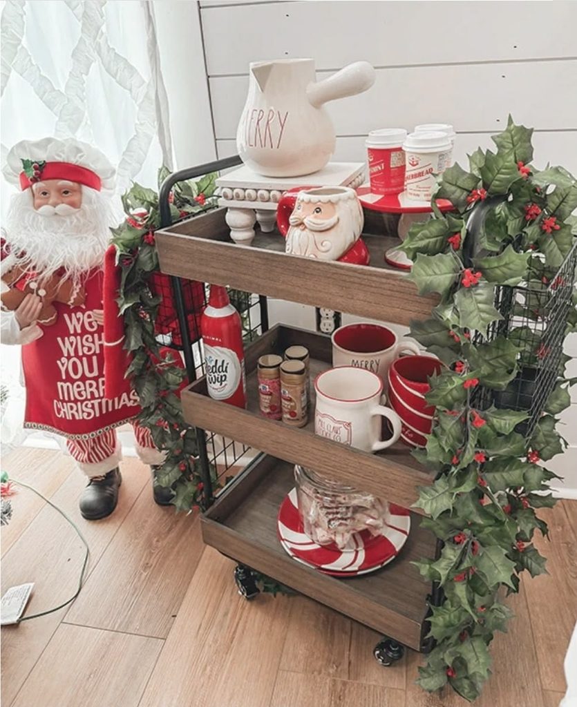 Three-tier rolling cart with red mugs, spice jars and whipped cream wrapped in a holly garland