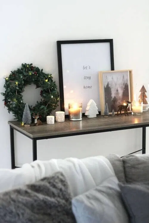 Christmas console table with a wreath, candles and mini trees behind a living room sofa