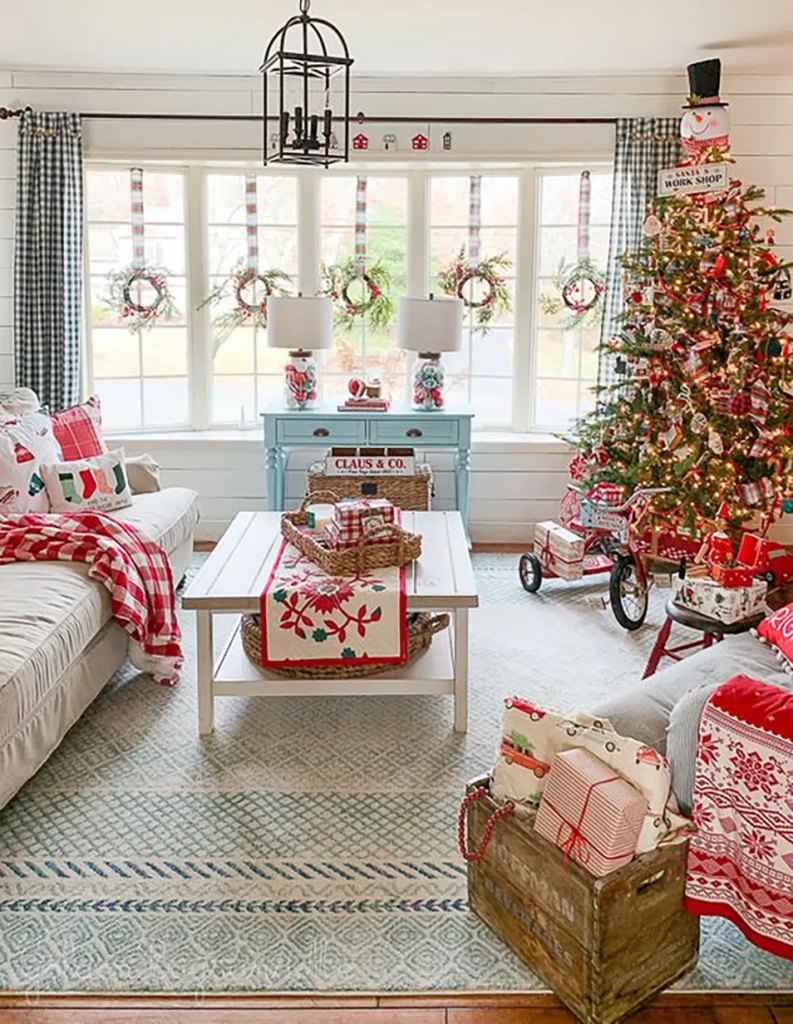 Small Christmas wreaths hanging in a living room bay window above a coffee table and sofa