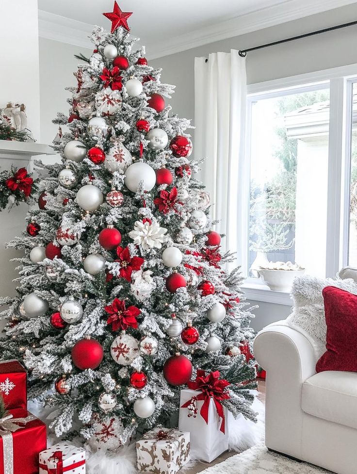 Red and white flocked Christmas tree with silver ornaments and poinsettias next to a white sofa.