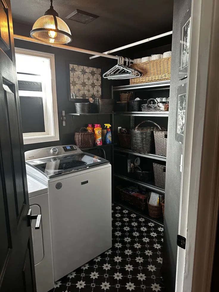Small laundry closet painted dark charcoal with a black door, a top-load washer, wire shelves with baskets and black-and-white star floor tile.