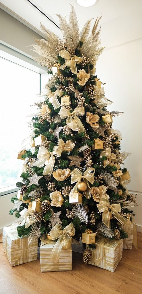 Glam gold Christmas tree with champagne ribbon bows, pinecones and a gold feather topper.