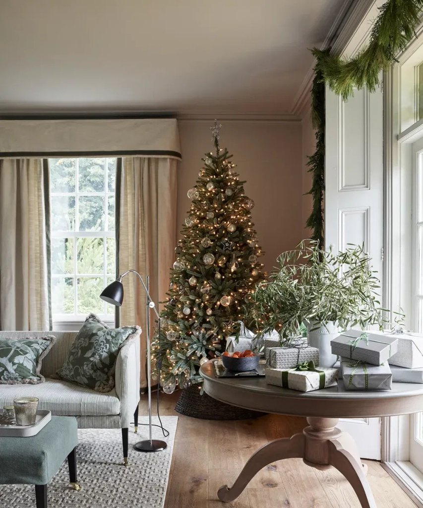 Green Christmas living room decor with a lit tree, olive branches in a vase and a green pillow on the sofa