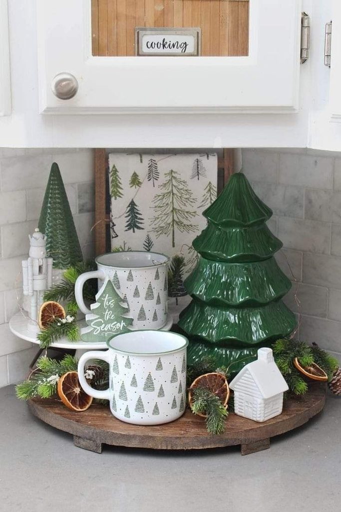 Green tree-print mugs and a green ceramic Christmas tree on a round wood tray in a kitchen corner