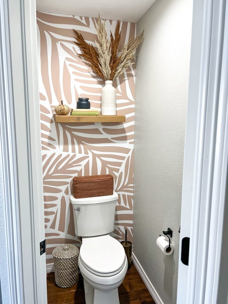 Peel-and-stick leaf wallpaper behind a toilet with a wood shelf, pampas grass and a wicker basket on the tank