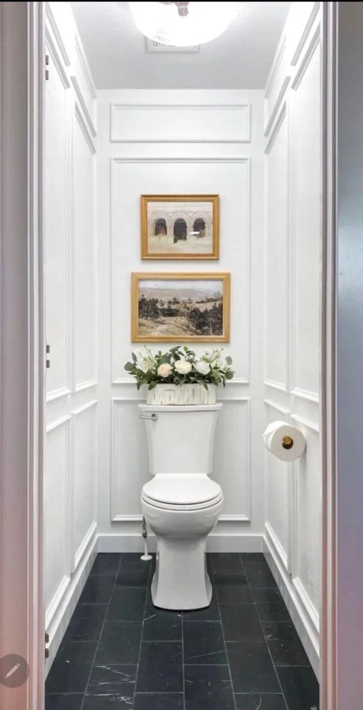 White picture frame molding on a narrow toilet room wall with two gold framed prints above the toilet