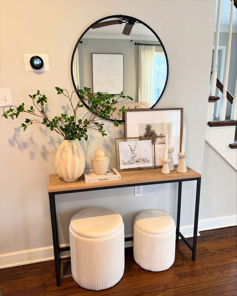 round black mirror above a slim console table with two cream stools underneath, small entryway table decor